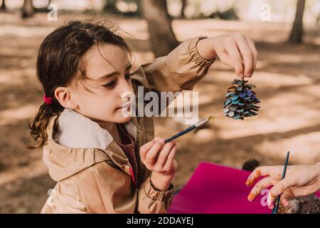 Cute girl holding pine cone while coloring by sister at park Stock Photo