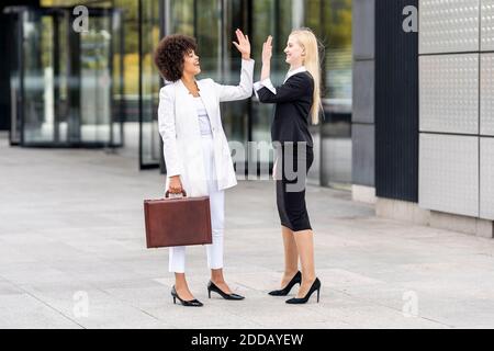 Businesswomen giving high five while standing on footpath Stock Photo