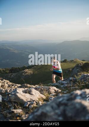 Man running on mountain trail against mountain range and clear sky Stock Photo