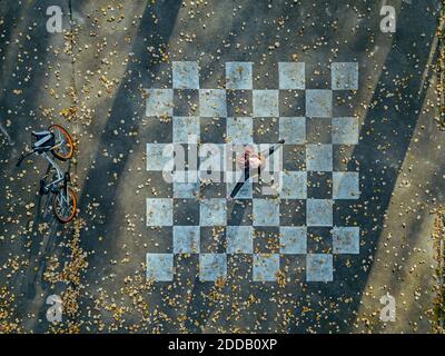 Woman with arms outstretched spinning on asphalt painted with chessboard pattern