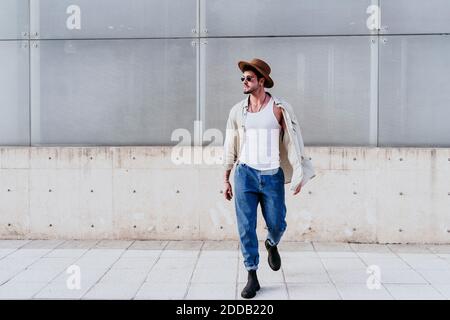 Confident man in hat looking away while walking against wall Stock Photo