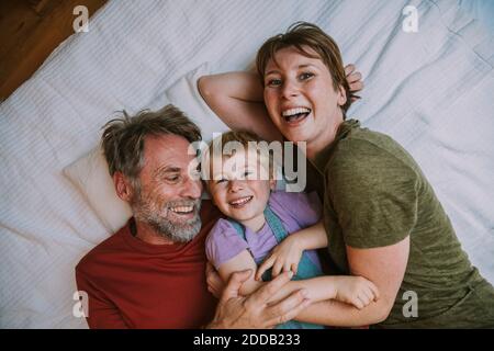 Smiling mother, father and son embracing each other while lying on bed at home Stock Photo