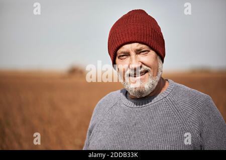 Farmer wearing knit hat smiling while standing at soybean farm Stock Photo