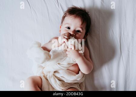 Cute baby boy holding towel while lying on bed in bedroom at home Stock Photo