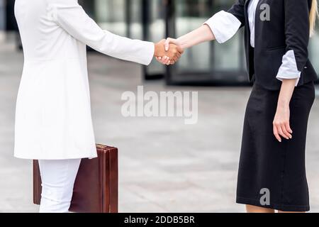Businesswomen doing handshake while standing on footpath Stock Photo