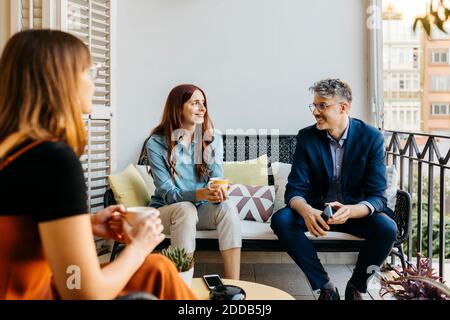 Smiling businesswoman discussing with coworkers while having coffee on sofa in balcony Stock Photo