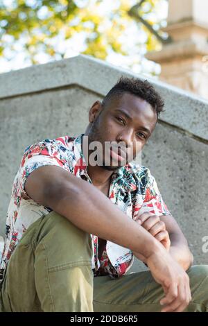 Serious young man sitting by retaining wall Stock Photo