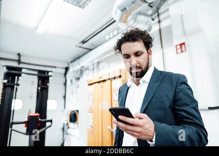 Male engineer using smart phone while standing at industry Stock Photo