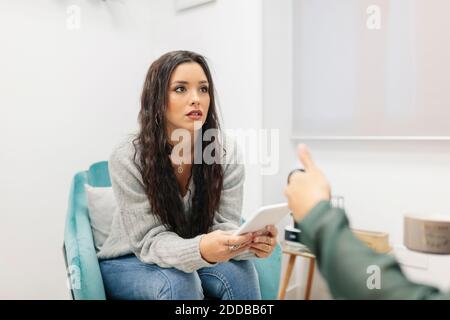Young woman using digital tablet while talking with doctor at office Stock Photo