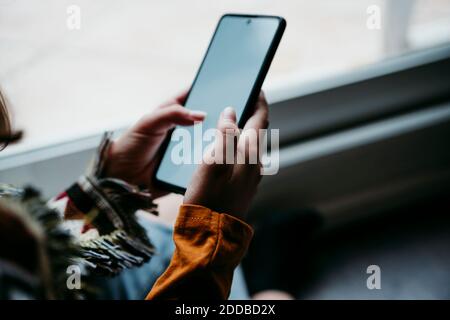 Girl using mobile phone while sitting by window at home Stock Photo