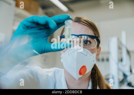 Young woman wearing protective face mask and eyeglasses examining test tube at laboratory Stock Photo