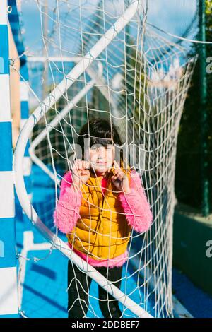 Cute girl leaning on goal post net at soccer court during sunny day Stock Photo