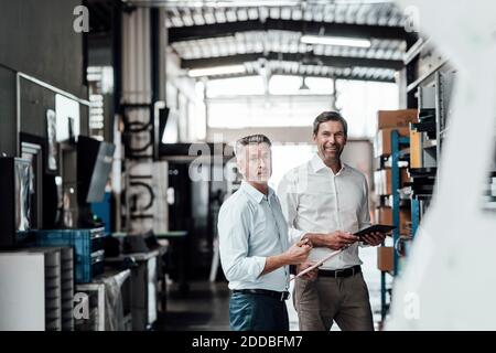 Smiling engineers with digital tablet standing in manufacturing industry Stock Photo