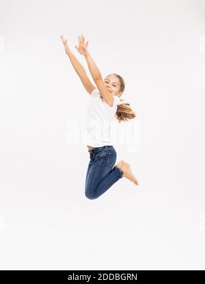 Cheerful girl jumping with arms raised near red wall Stock Photo - Alamy