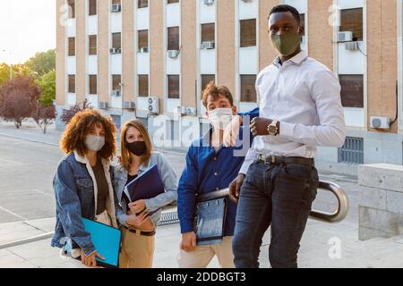University students wearing protective face mask while standing on staircase against education building Stock Photo
