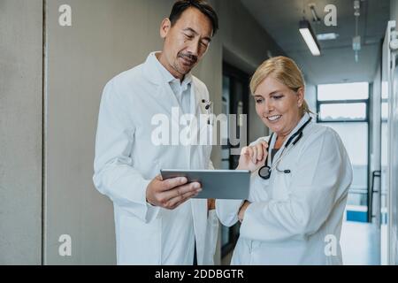 Smiling scientist and doctor using digital tablet while standing at clinic corridor Stock Photo