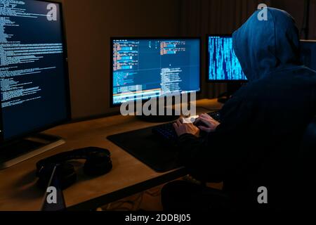 Hacker wearing hoodie working on computer while sitting at office Stock Photo