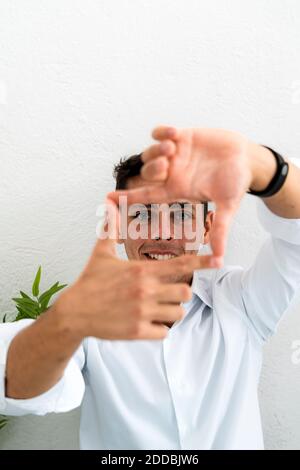 Smiling businessman making square shape from fingers and thumbs against white wall at office Stock Photo