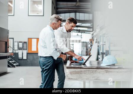 Male engineers discussing over laptop at table in industry Stock Photo