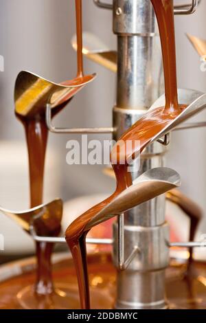 Chocolate fountain in use at catering event.  Filled with dark chocolate flowing down. Shallow focus, liquid chocolate dessert flowing. Stock Photo