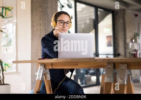 Businesswoman wearing headphones using laptop while sitting by table at office Stock Photo