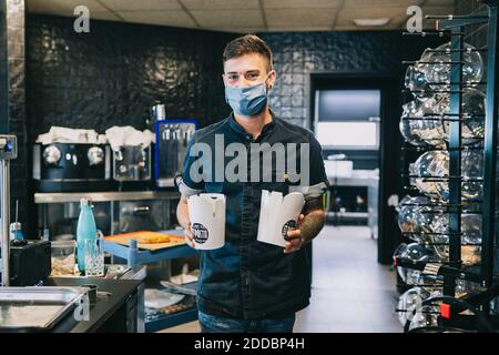 Mid adult male chef holding take out food containers at restaurant kitchen during pandemic Stock Photo