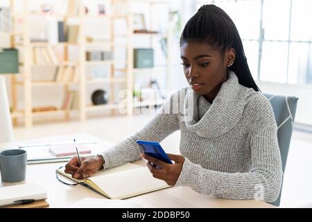 Female student using smart phone while studying at home Stock Photo