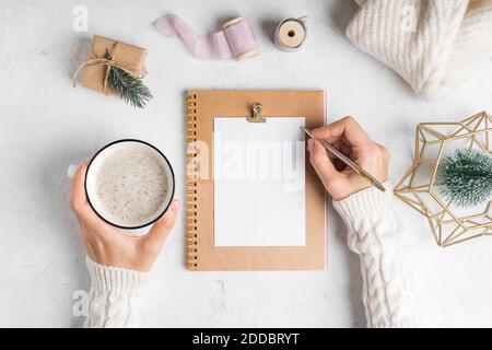 Desktop of woman hands writing in blank notepad. Flat lay of white working table background with cup of coffee and Christmas decoration. Top view, moc Stock Photo