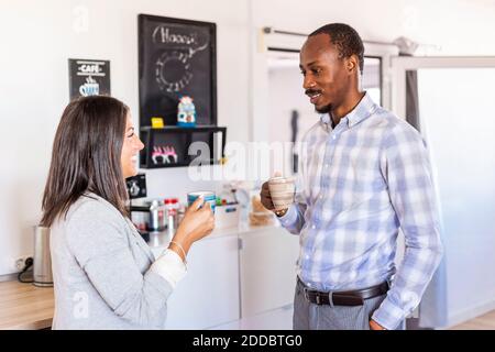 Smiling male and female entrepreneurs talking while having coffee during break in office Stock Photo