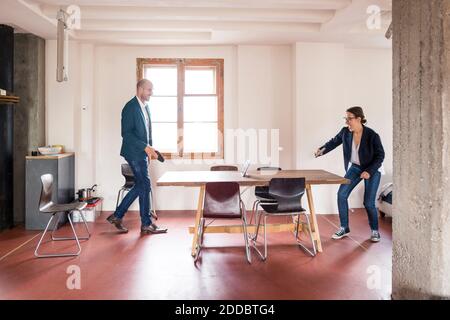 Carefree man and woman playing table tennis while standing at office Stock Photo