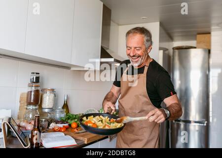 Smiling mature man preparing pasta while standing in kitchen at home Stock Photo