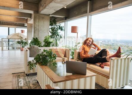 Man reading book with hand in hair sitting on sofa at home Stock Photo