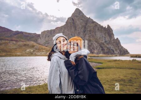 Sisters wearing warm clothing embracing while standing against lake at Ibones of Anayet Stock Photo