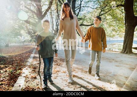 Happy mother and sons walking in public park on sunny day Stock Photo