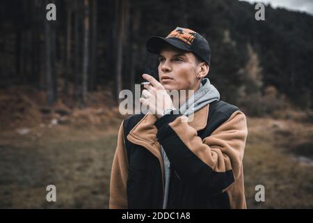 Young man looking away while smoking standing in forest during autumn Stock Photo