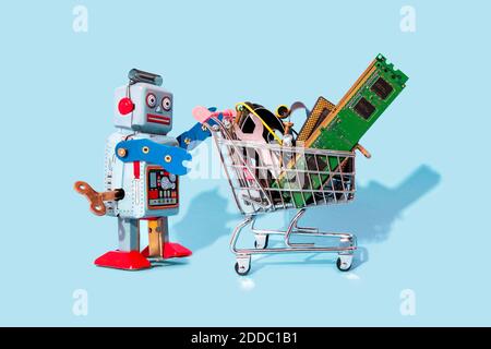 Studio shot of vintage robot toy pushing miniature shopping cart filled with electronic equipment Stock Photo