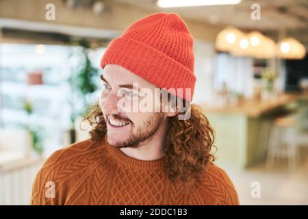 Smiling hipster man wearing red knit hat at home Stock Photo