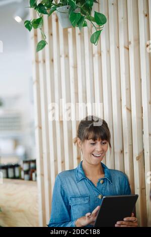 Female owner using digital table standing against wooden wall Stock Photo