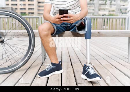 Low section of man with artificial limb using mobile phone in city Stock Photo