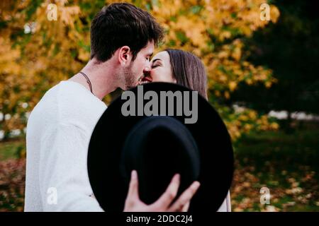 Man with hat kissing smiling female partner while standing outdoors Stock Photo