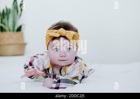 Baby girl wearing head bow playing while lying on bed at home Stock Photo