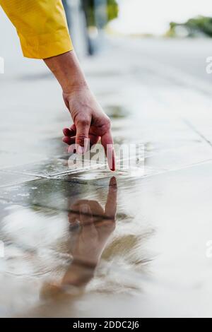 Woman' hand touching rain puddle on street Stock Photo