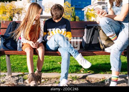 Low section of mother with smiling kids using smart phone while sitting on bench in public park Stock Photo