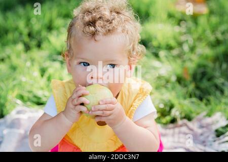 Cute baby girl eating fruit while sitting on grass at park Stock Photo