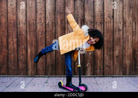 Playful girl riding push scooter against wooden wall Stock Photo