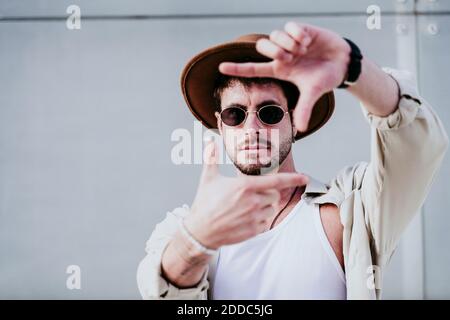 Thoughtful man in hat and sunglasses gesturing against wall Stock Photo