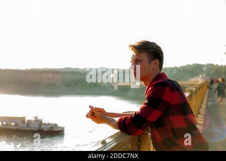 Contemplating man looking away while standing by railing on bridge against clear sky Stock Photo