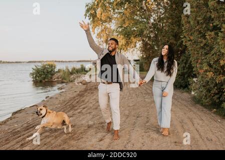 Woman looking at boyfriend playing with dog while walking by lake Stock Photo