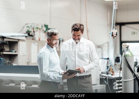 Mature male engineers discussing over digital tablet while standing in manufacturing industry Stock Photo