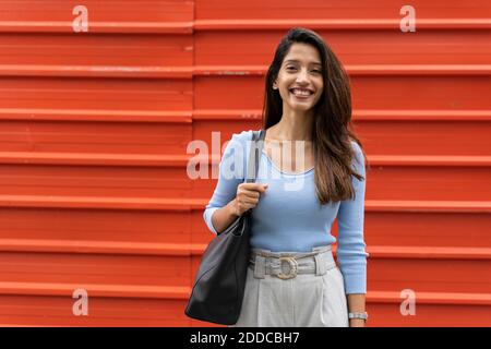 Smiling confident woman with purse standing against shutter Stock Photo